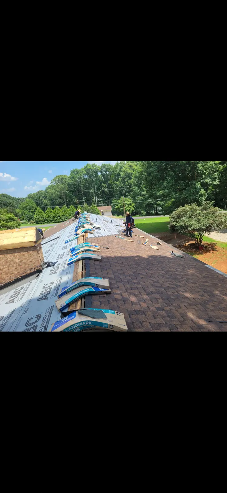 Roofers laying shingles along the ridge of a roof