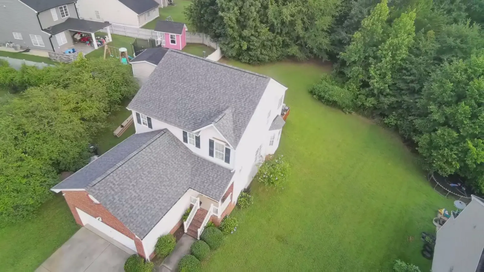 Drone view of a finished gray shingle roof on a white two story home