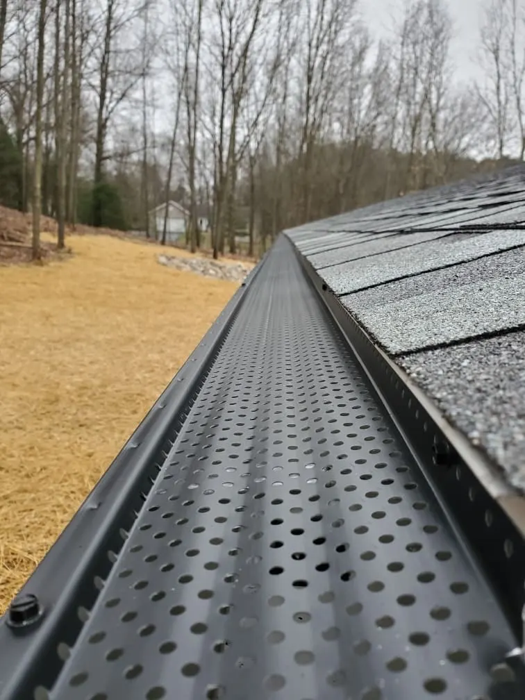 Close up of a perforated gutter guard fitted along a shingle edge