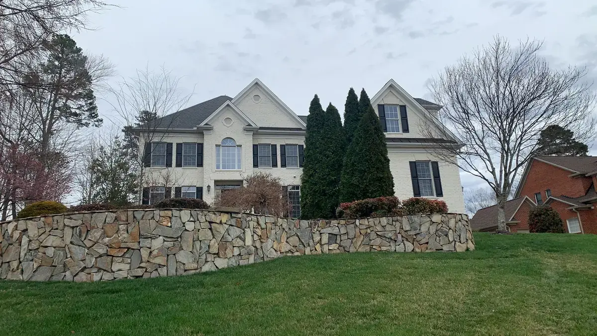 Large two story home behind a stone retaining wall with its completed roof
