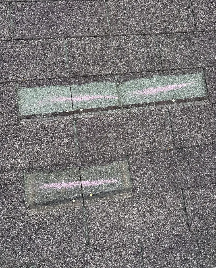 Chalk lines drawn across three shingle tabs with nail heads showing