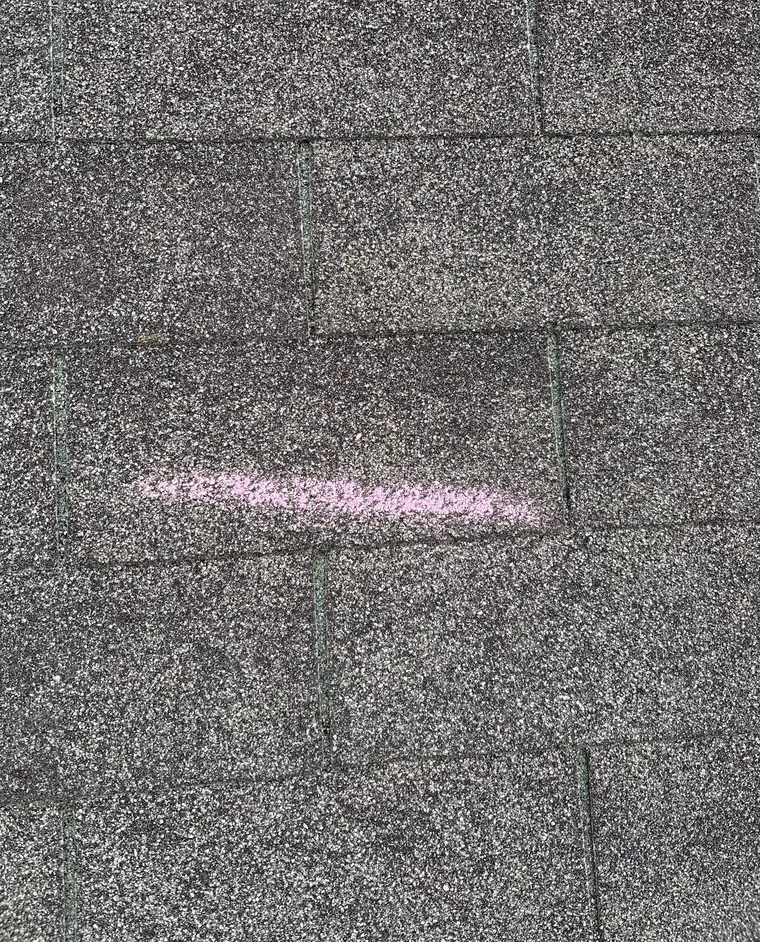 A short chalk line marked on gray asphalt shingles
