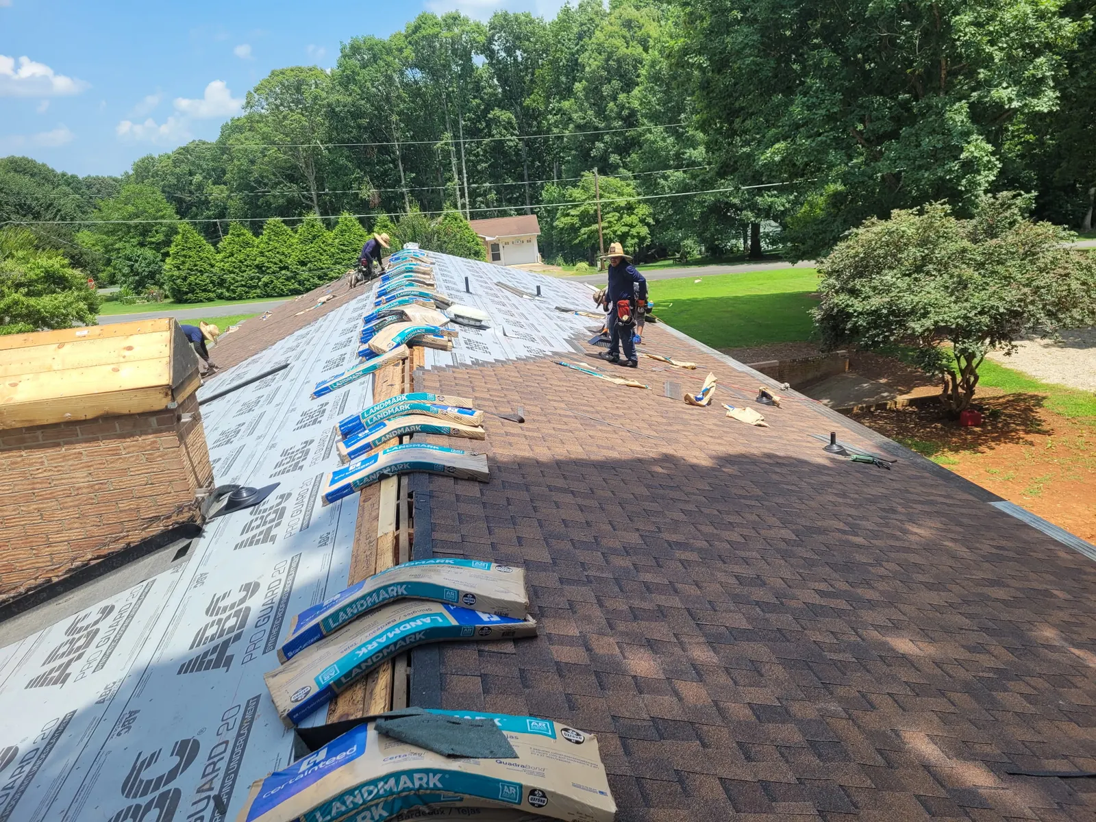 Crew laying CertainTeed Landmark shingles halfway across a roof, bundles staged along the ridge