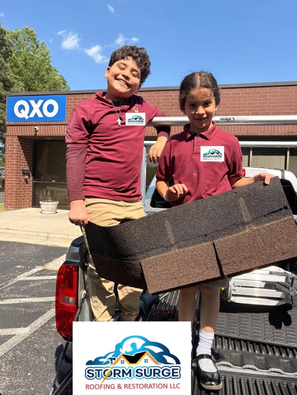 Two kids in Storm Surge shirts holding a shingle in the truck bed on a supply run