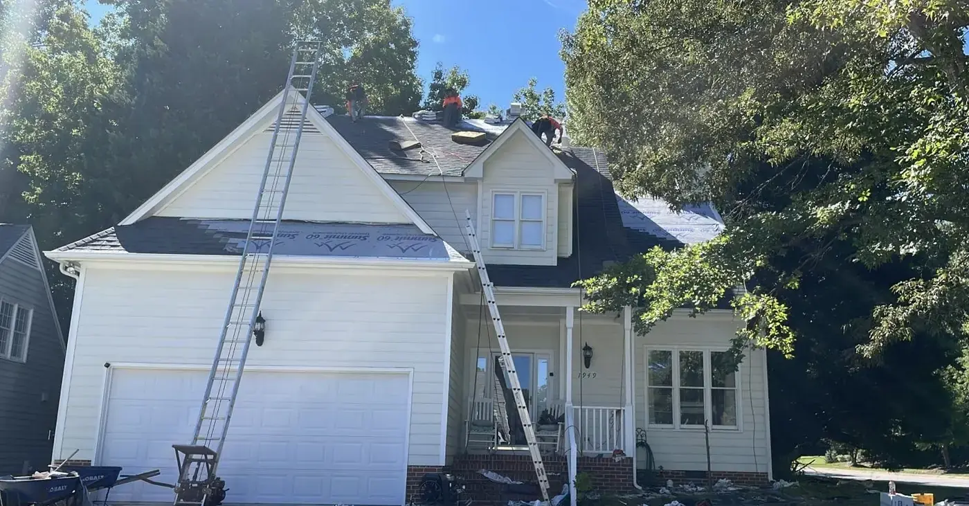 Crew stripping the old shingles from a white two story house with ladders up both slopes